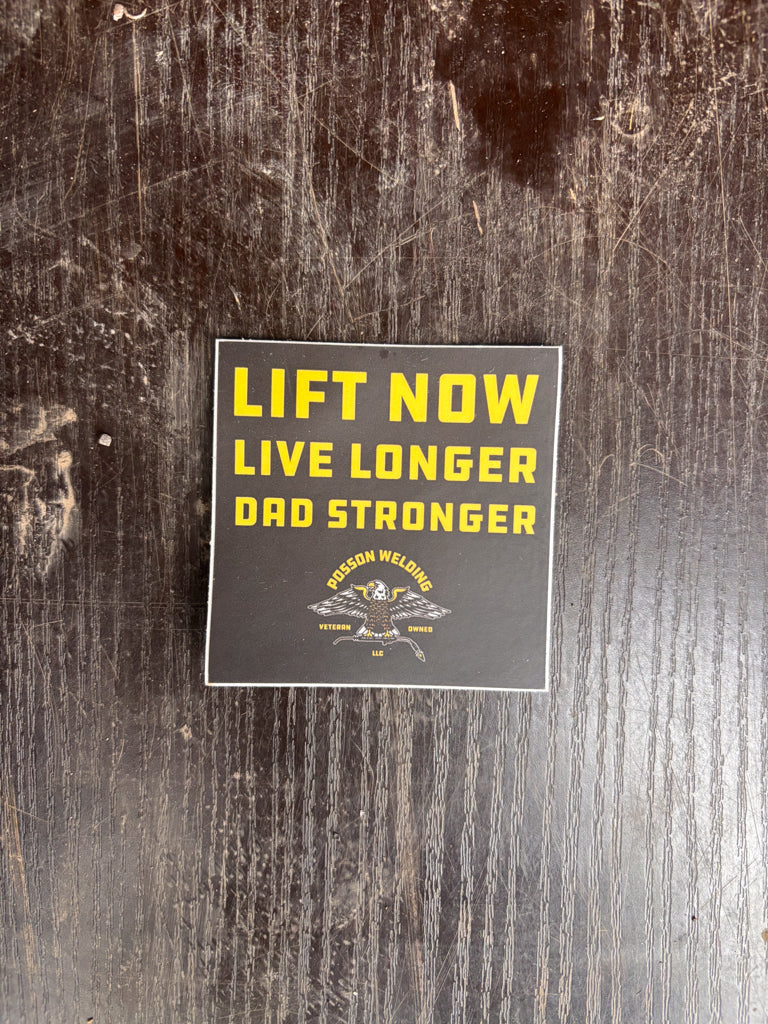 Sticker with text 'Lift Now Live Longer Dad Stronger' on a wooden surface