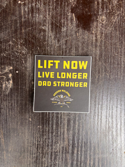 Sticker with text 'Lift Now Live Longer Dad Stronger' on a wooden surface